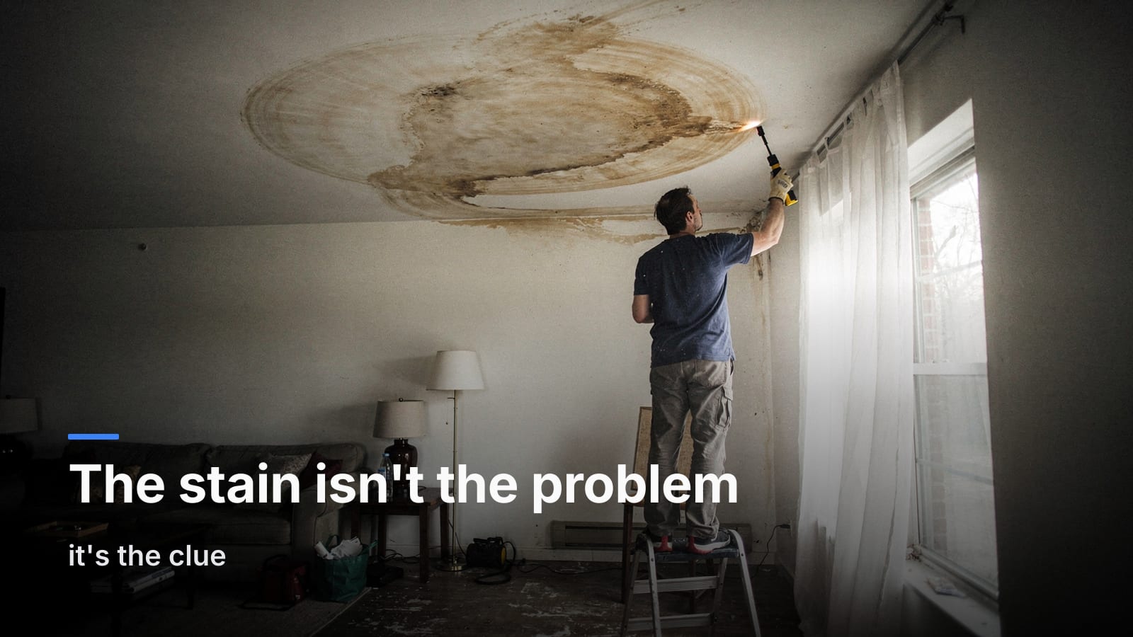 Homeowner on a step stool shining a flashlight at a brown ring-shaped water stain on a white ceiling.